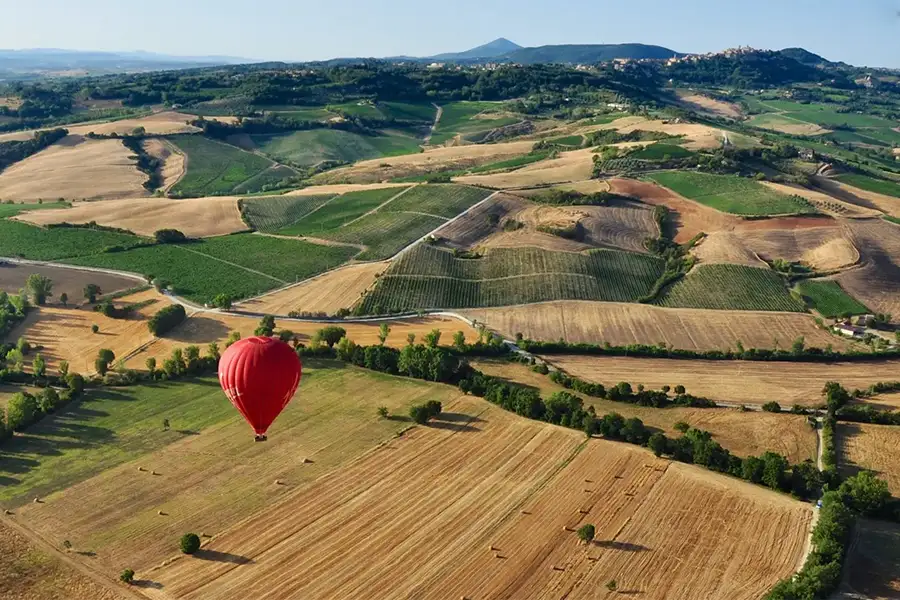 Balão de ar quente vermelho sobrevoando as colinas e campos cultivados da Toscana, com vista panorâmica da paisagem rural