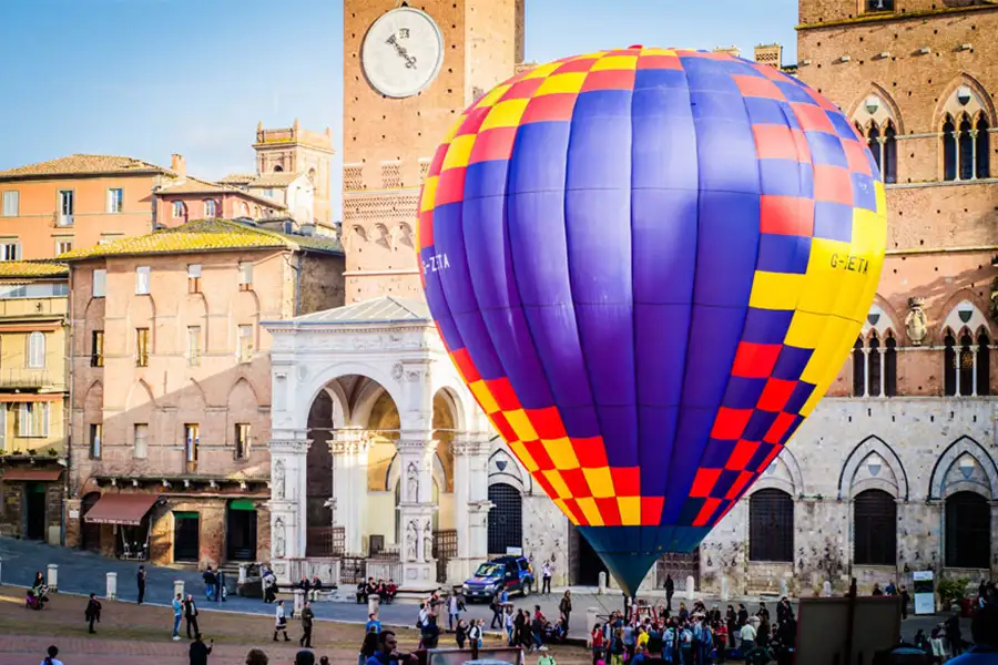 Balão de ar quente colorido montado na Piazza del Campo, em Siena, com edifícios históricos e a Torre del Mangia ao fundo