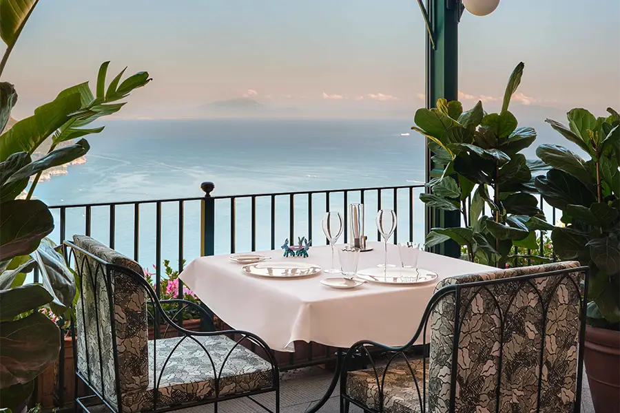 Mesa ao ar livre elegantemente posta com vista para o mar Mediterrâneo, cercada por plantas no terraço do restaurante Palazzo Avino, na Costa Amalfitana